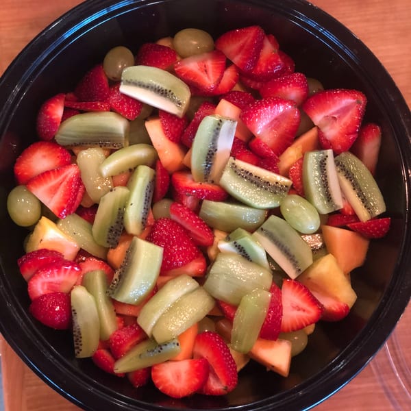 A black bowl filled with a colorful fruit salad of sliced strawberries, kiwi, grapes, and cantaloupe.