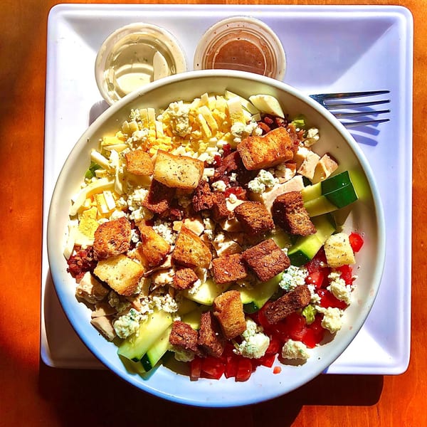 A vibrant Cobb salad with chicken, egg, bacon, blue cheese, tomatoes, cucumbers, and croutons.