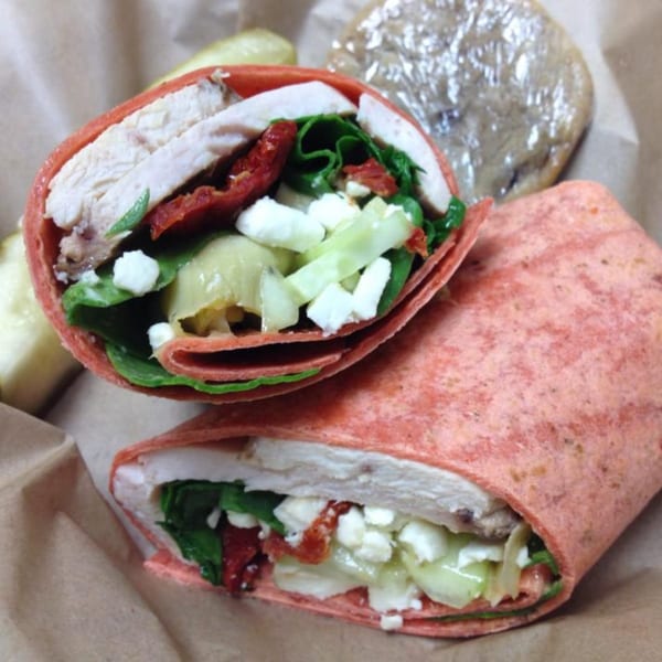 Two Knickerbockers Deli chicken wraps with sun-dried tomatoes, feta, and greens, with a pickle and cookie.