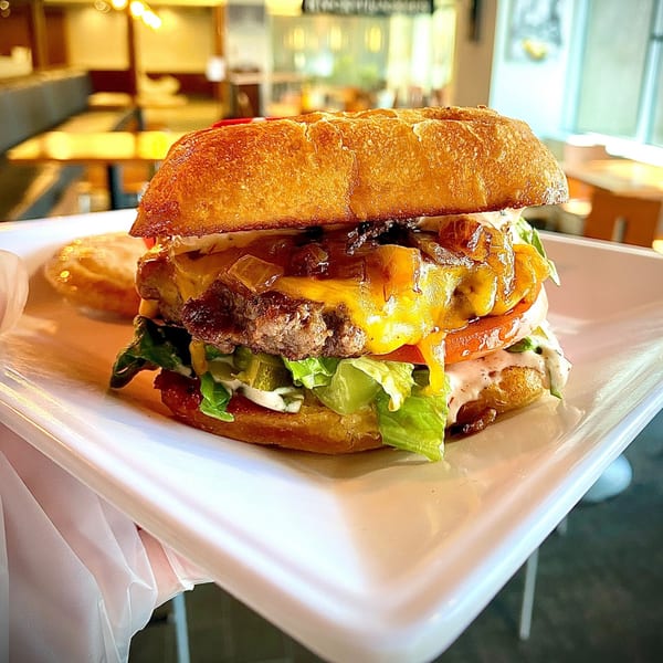 A Knickerbockers Deli burger with melted cheese, caramelized onions, lettuce, tomato, and sauce.