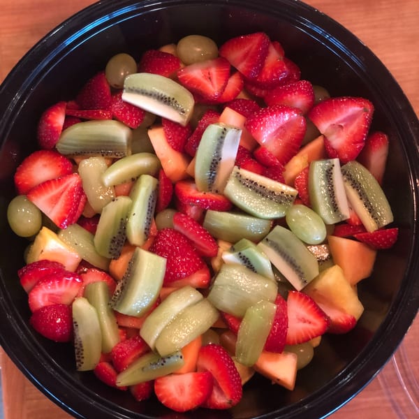 A black bowl filled with a colorful fruit salad of sliced strawberries, kiwi, grapes, and melon.