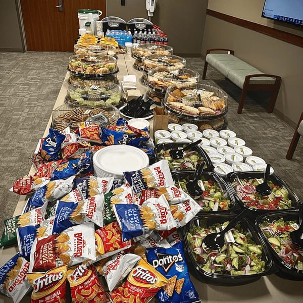 A long table filled with Knickerbockers Deli sandwich platters, salads, chips, and drinks for catering.