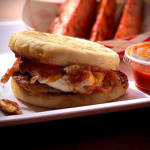 Knickerbockers Deli breakfast sandwich with egg, bacon, and cheese, served with hot sauce.
