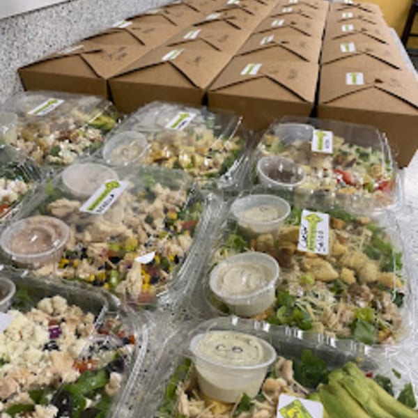 Numerous catering boxes and clear containers of salads with dressing cups, ready for delivery from Knickerbockers Deli.