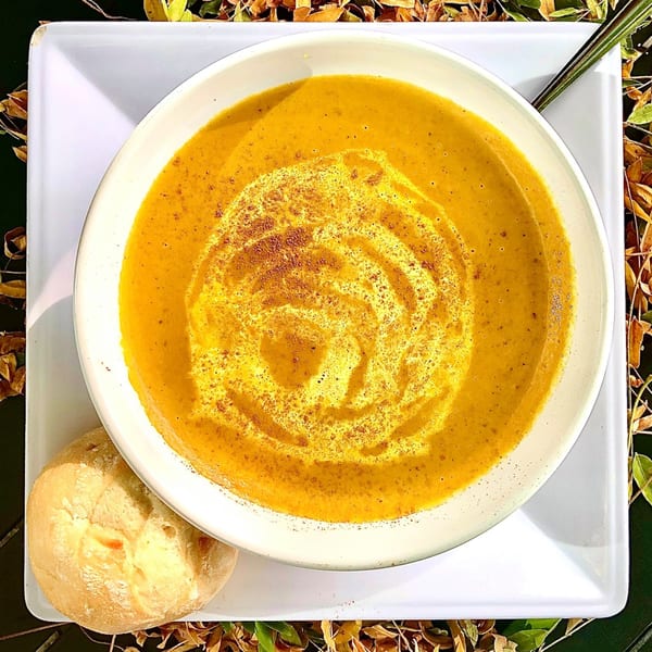 Overhead view of a bowl of orange soup with a cream swirl and a bread roll.