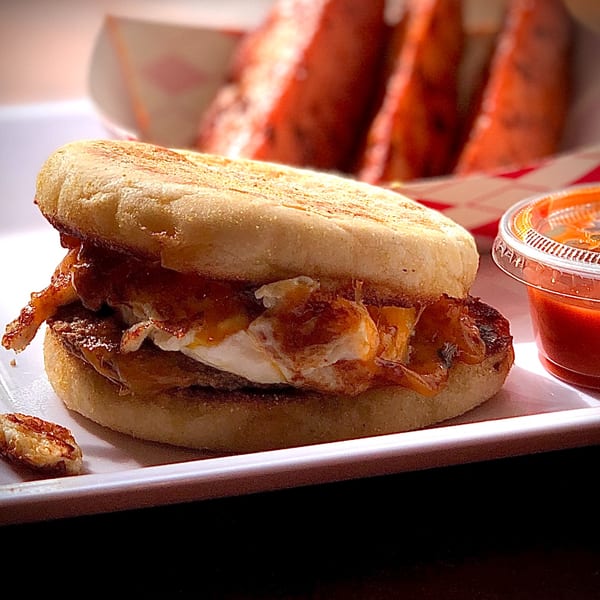 Knickerbockers Deli breakfast sandwich with egg and bacon, served with a side of sauce and watermelon.