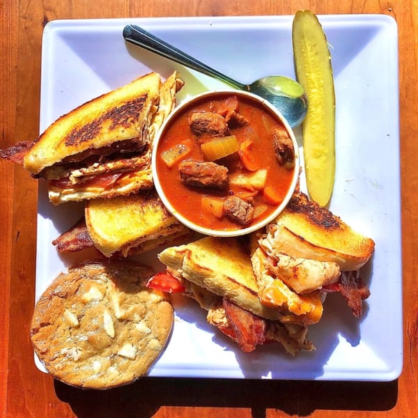 Knickerbockers Deli sandwich with soup, pickle, and cookie on a white plate.