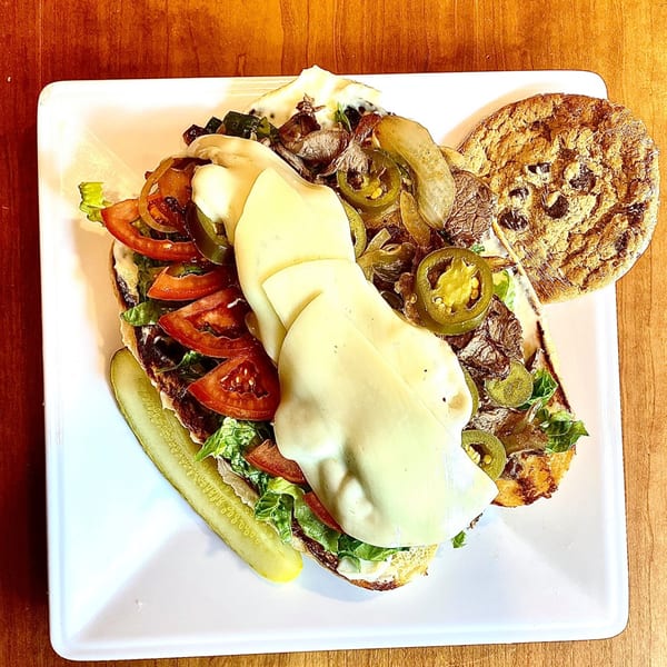 Knickerbockers Deli steak sandwich with melted cheese, jalapenos, lettuce, tomato, and a pickle spear.